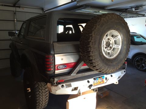 1988 Ford Bronco - The rear passenger side of a dark colored Ford Bronco is shown parked in a garage. It features a large spare tire mounted on the back, a cu…