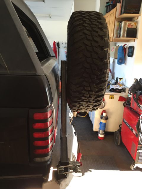 1988 Ford Bronco - A black SUV's rear corner and spare tire mounted on a carrier are visible in a garage setting. The spare tire is large and aggressive, moun…
