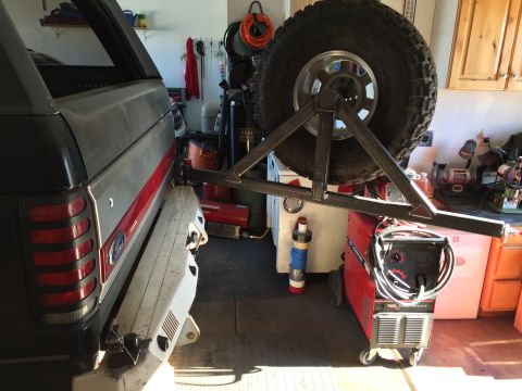 1988 Ford Bronco - The rear passenger side of a dark gray Ford Bronco with a red stripe is shown. A custom metal spare tire carrier is mounted to the rear bum…