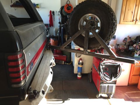 1988 Ford Bronco - The rear driver's side of a black and silver Ford Bronco with a red stripe is shown, fitted with a custom-built swing-away spare tire carri…