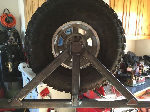 1988 Ford Bronco - A large off-road tire is mounted on a custom metal fabrication stand, likely for a vehicle. The stand is constructed from square steel tubi…