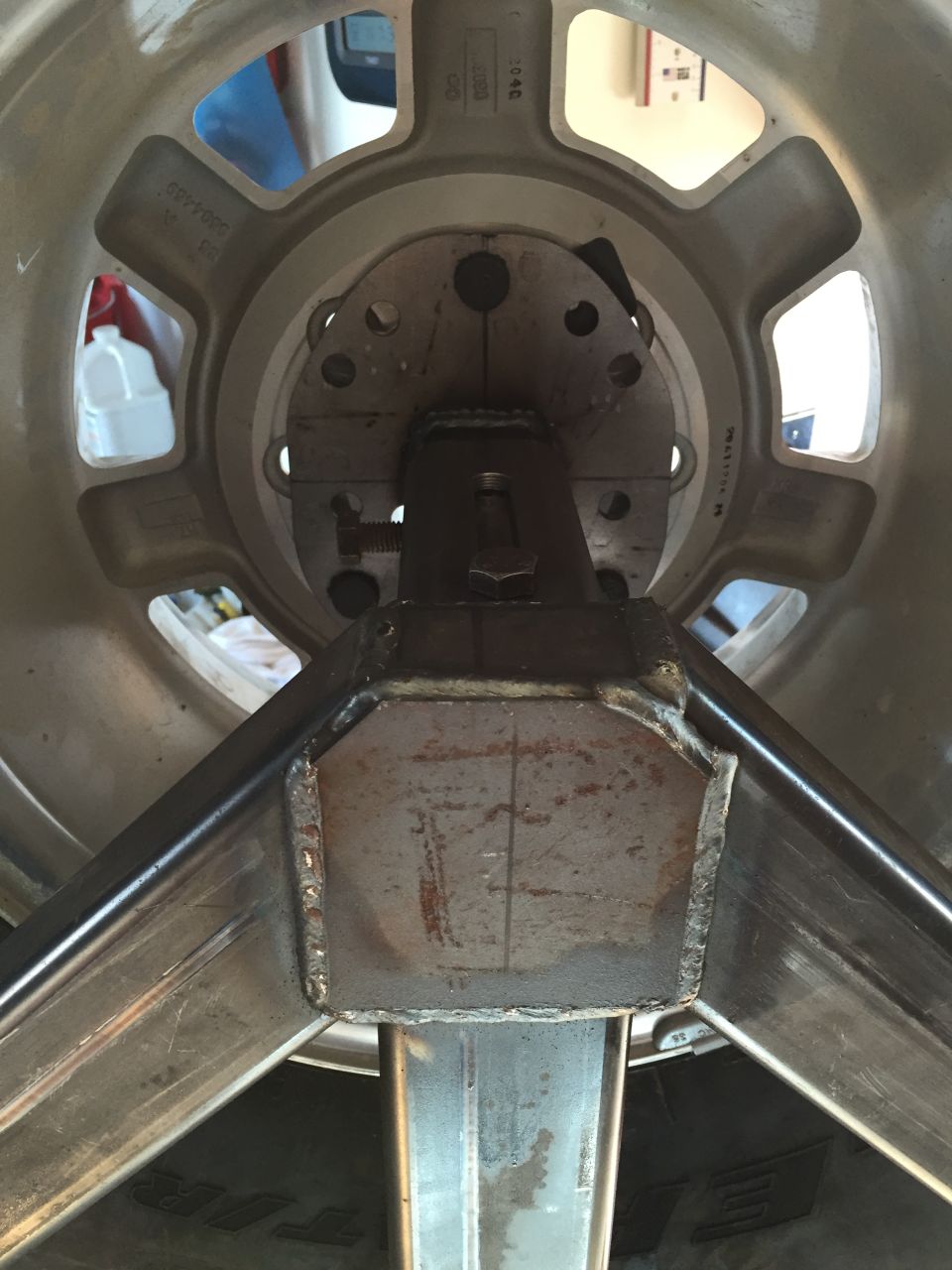 Custom metal jig attached to a vehicle wheel hub, showing welds and tubing.
