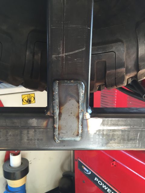 1988 Ford Bronco - A close-up view shows a welded metal bracket attached to a thick horizontal metal beam, with a portion of a large tire visible above. The s…