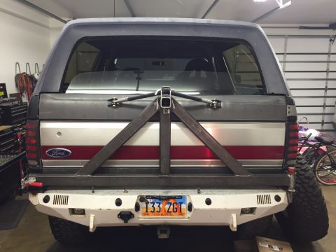 1988 Ford Bronco - The rear of a Ford Bronco is shown with a custom-fabricated steel spare tire carrier and bumper. The vehicle has a two-tone paint scheme wi…