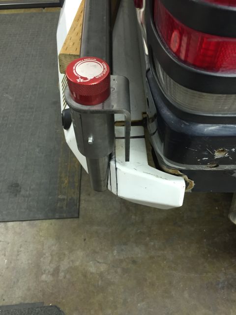 1988 Ford Bronco - A close-up view shows a custom metal bracket mounted to the rear bumper of a white vehicle, holding a red knurled cap with text. The vehicl…