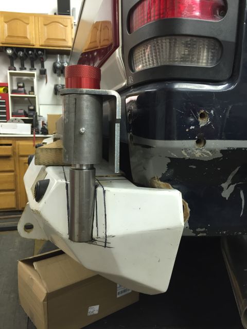 1988 Ford Bronco - A custom white bumper is being fitted to the rear corner of a dark blue SUV, with a metal bracket and red cap visible. The bumper has black…
