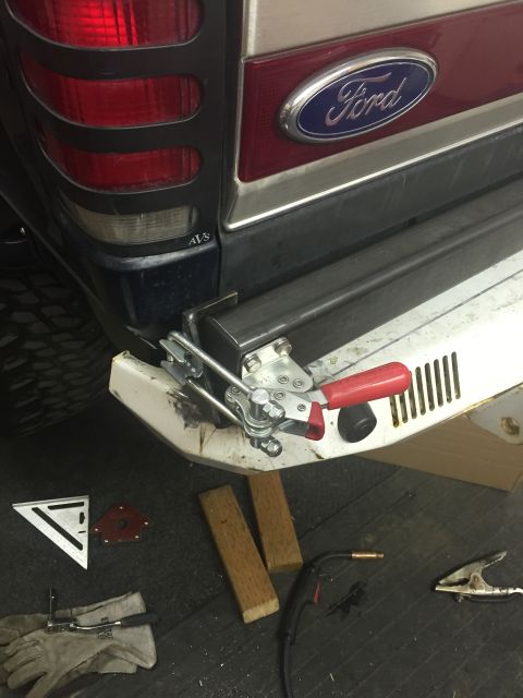 1988 Ford Bronco - A close-up rear view of a Ford SUV's taillight and bumper area, showing a metal bumper modification in progress. Welding equipment and tool…