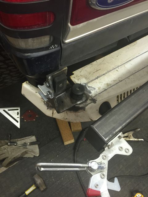 1988 Ford Bronco - A close-up view of a custom metal bumper being fabricated and attached to the rear corner of a dark blue SUV. Various tools and parts are l…