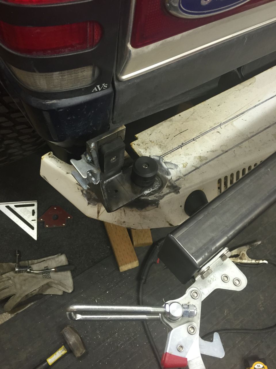 Custom bumper fabrication on a dark blue SUV rear corner, with tools on the ground.