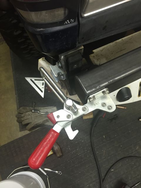 1988 Ford Bronco - A close-up view of a vehicle's rear bumper area, showing a clamp tool attached to a metal bracket and a portion of the vehicle's dark blue…