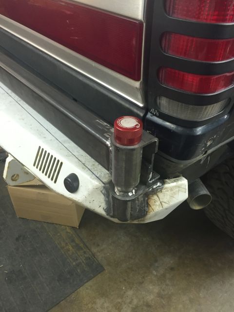 1988 Ford Bronco - A close-up view of the rear bumper area of a vehicle, showing custom metal fabrication and a red cap with white lettering. The vehicle appe…