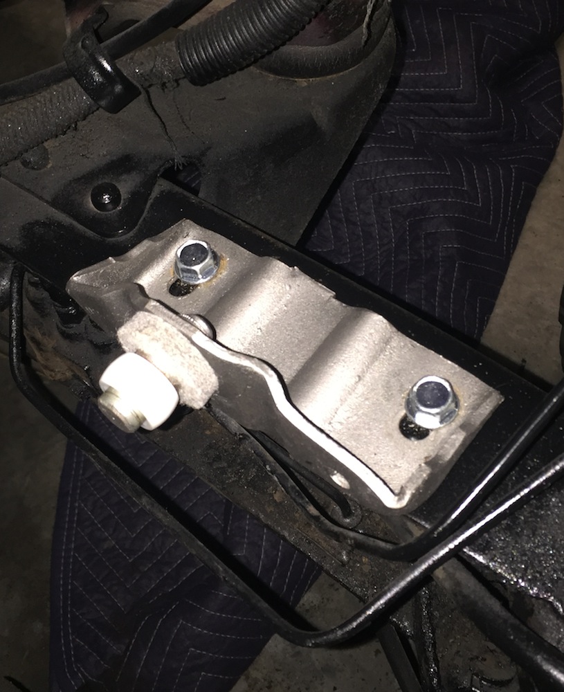 Close-up of a metal bracket bolted to a vehicle frame, with a quilted blanket below.