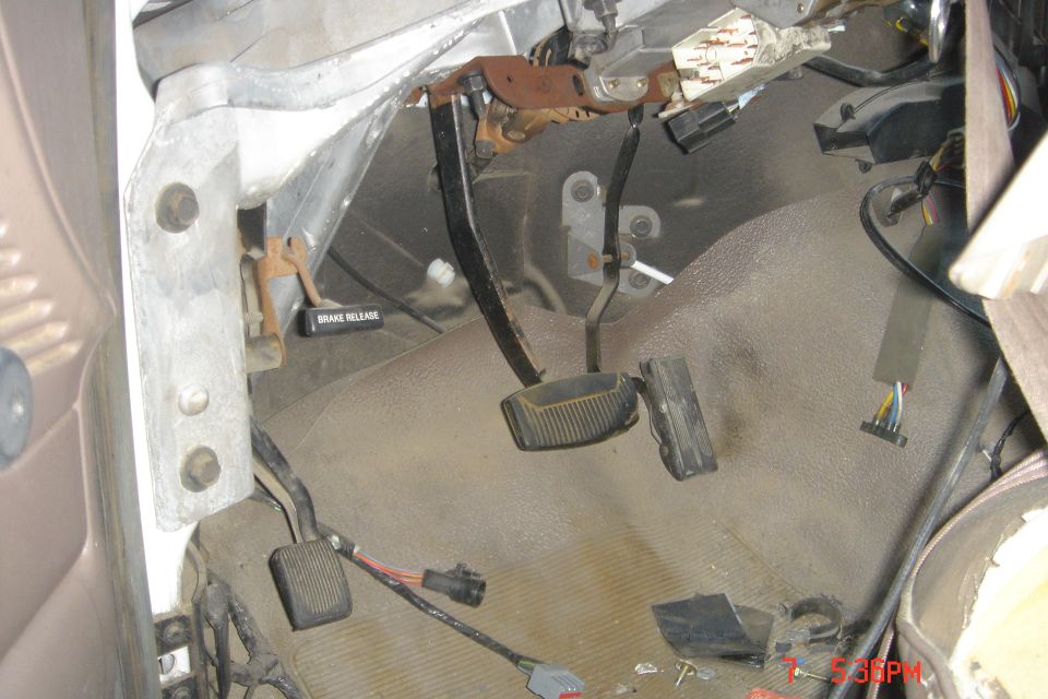 Vehicle interior footwell with brake and clutch pedals, and wiring.