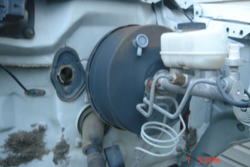 Brake booster and master cylinder assembly with white reservoir on a vehicle firewall.