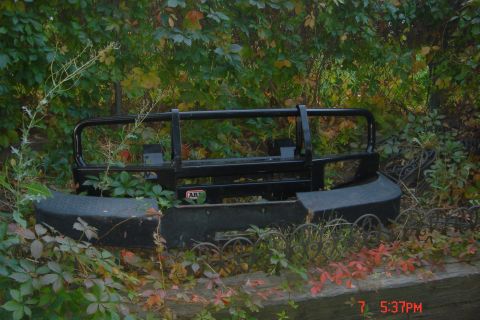 1988 Ford Bronco - A black aftermarket bumper is partially obscured by foliage and vines. The bumper has a visible "ART" logo on the driver's side.