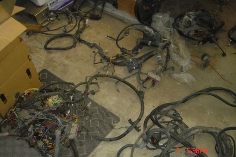 1988 Ford Bronco - A pile of vehicle wiring harnesses and electrical components are spread out on a concrete floor next to cardboard boxes. One harness is par…
