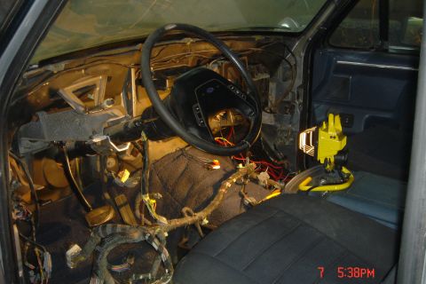 1988 Ford Bronco - The interior of a disassembled vehicle, likely a truck or SUV, shows the dashboard, steering wheel, and exposed wiring. A yellow work light…