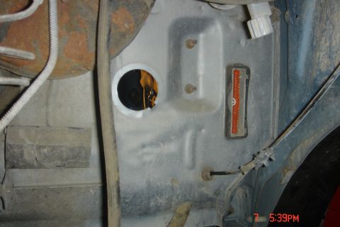 1988 Ford Bronco - A close-up view of a vehicle's undercarriage, showing a metal panel with a circular opening, a wiring harness, and a multi-pin connector. S…