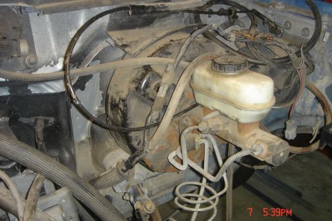 1988 Ford Bronco - A close-up view of the brake master cylinder and brake booster assembly in a vehicle engine bay. The components are covered in dust and gri…