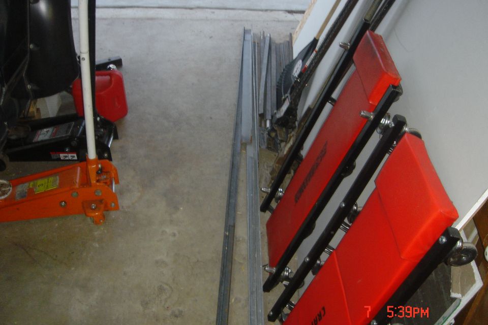Red creeper seat leaning against a wall, with a floor jack and gas can on the floor.