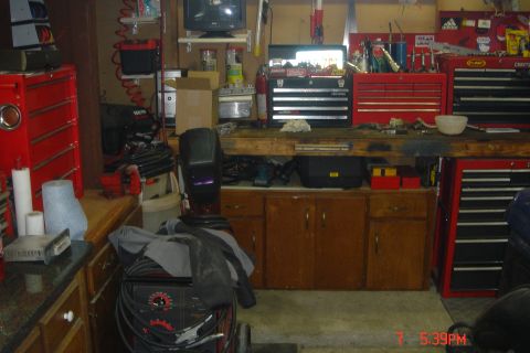 1988 Ford Bronco - This image shows a cluttered garage workshop with various tools and equipment, including a welding machine, toolboxes, and a welding mask.…