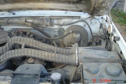 1988 Ford Bronco - The engine bay of a white Ford Bronco is shown, with the hood open. The engine is covered in dust and grime, with various hoses and compone…