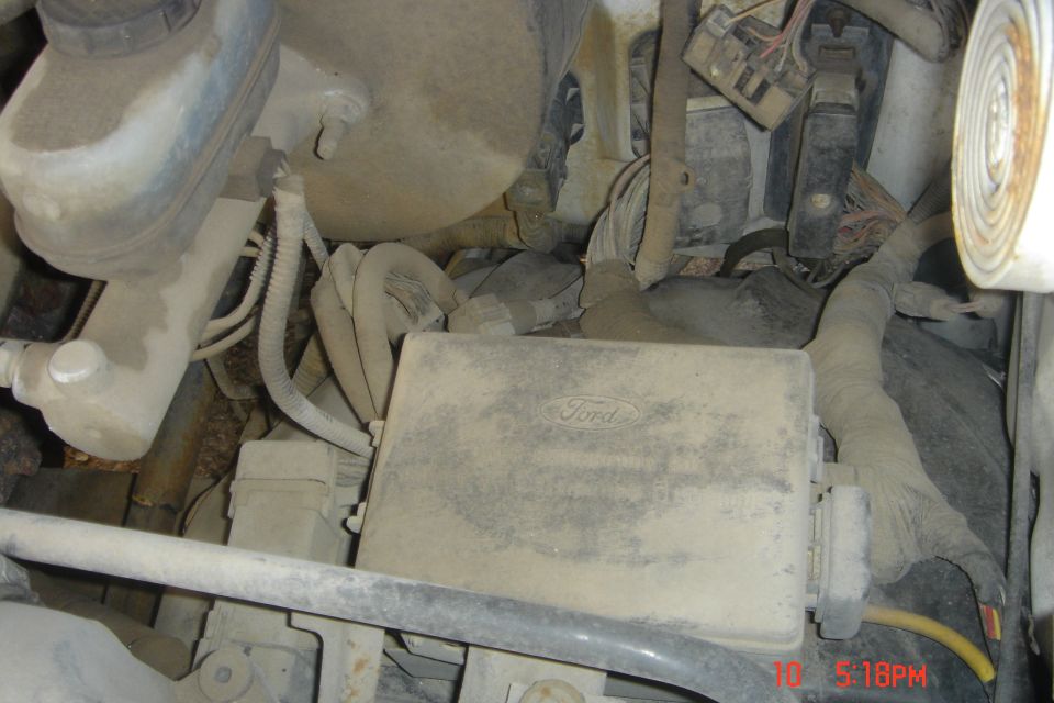 Dusty Ford fuse box and brake fluid reservoir in a vehicle engine bay.