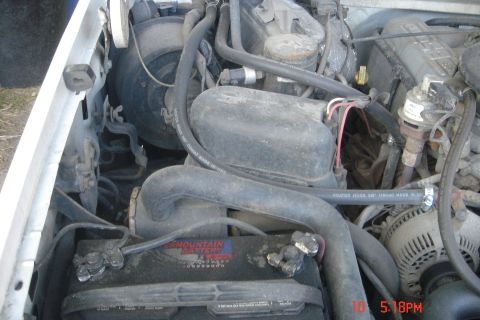 1988 Ford Bronco - A close-up view of the engine bay of a white Ford Bronco, focusing on the battery and various hoses and engine components. The battery is l…