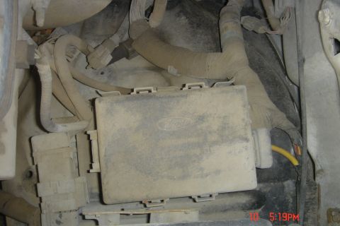 1988 Ford Bronco - A dusty, gray plastic fuse box with a Ford logo is visible in the engine bay, surrounded by various wires and conduits.