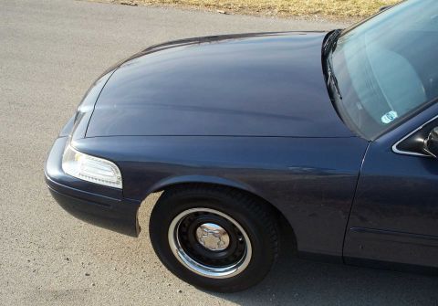 1998 Ford Crown Victoria - A dark blue 1998 Ford Crown Victoria is shown from the front quarter panel, revealing its classic body style.