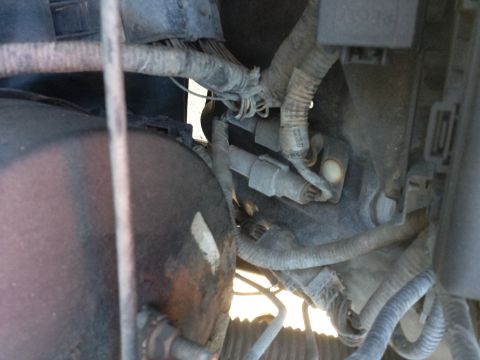 1988 Ford Bronco - This close-up photo shows a complex wiring harness and a portion of a round, dark-colored component, possibly a brake booster or reservoir,…