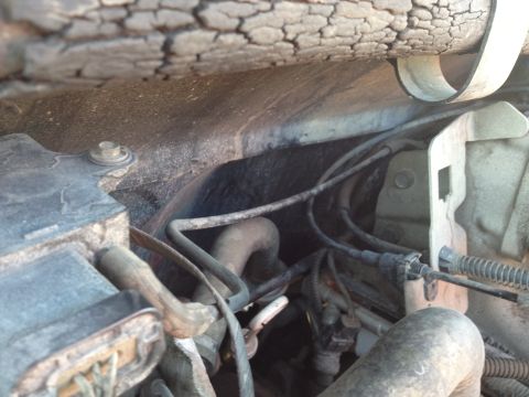 1988 Ford Bronco - A close-up view of the engine bay of a 1988 Ford Bronco, showing various hoses, wires, and a metal bracket. The area appears dusty and worn…