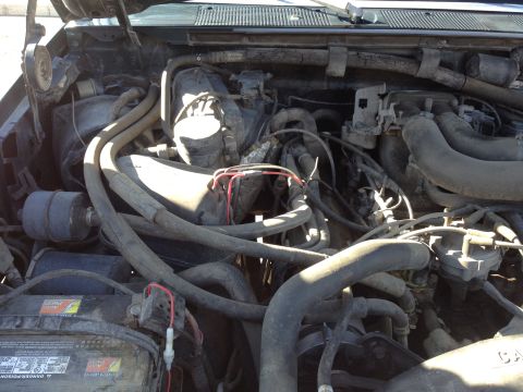 1988 Ford Bronco - This is a close-up, overhead view of a dusty engine bay, likely from a 1988 Ford Bronco, showing various hoses, wires, and the battery.