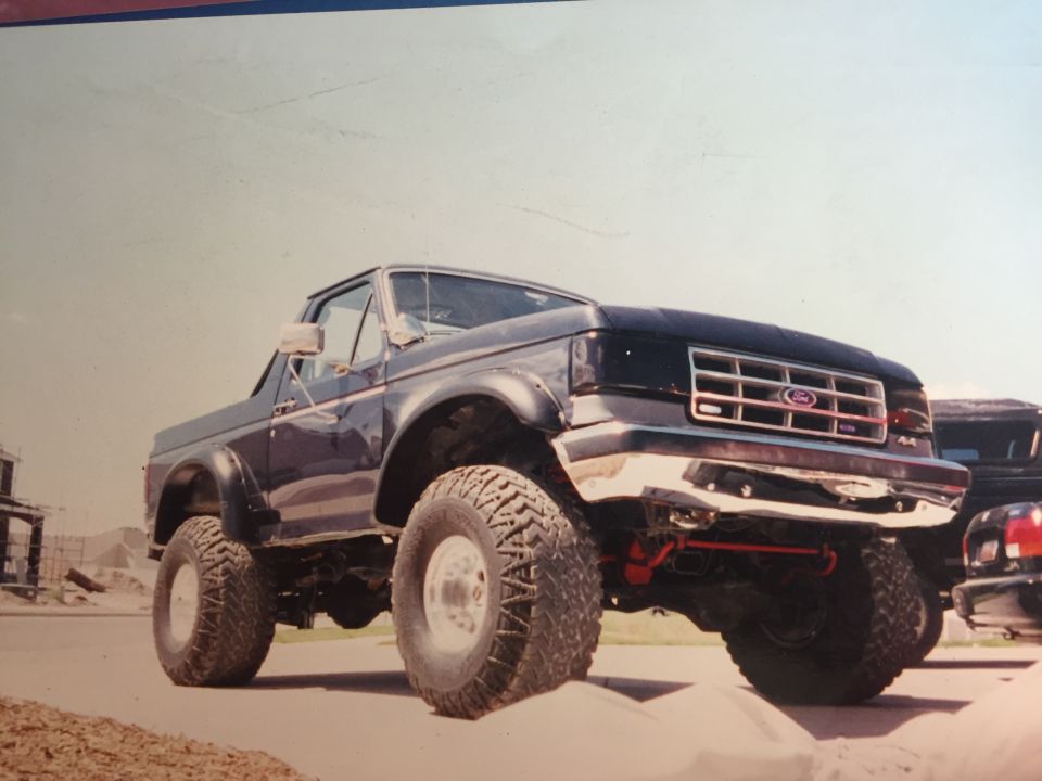 Lifted dark blue 1988 Ford Bronco with large off-road tires and chrome bumper.