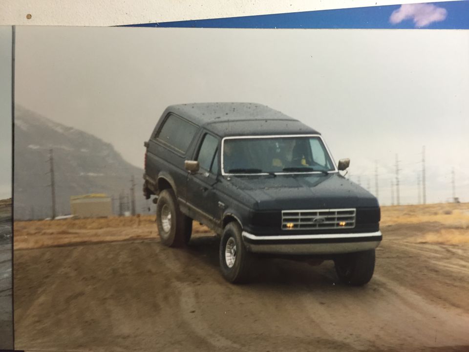 1988 Ford Bronco driving on a dirt road with mountains in the background.