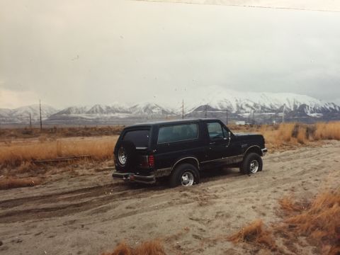 1988 Ford Bronco - A black, two-door Ford Bronco is stuck in sandy terrain with snow-capped mountains in the background.