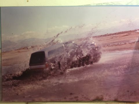 1988 Ford Bronco - A dark-colored SUV drives through a muddy, watery area, kicking up a large splash. The vehicle is viewed from the rear quarter angle in an…