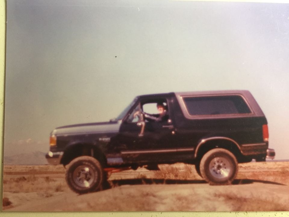 1988 Ford Bronco parked on dirt with driver visible.