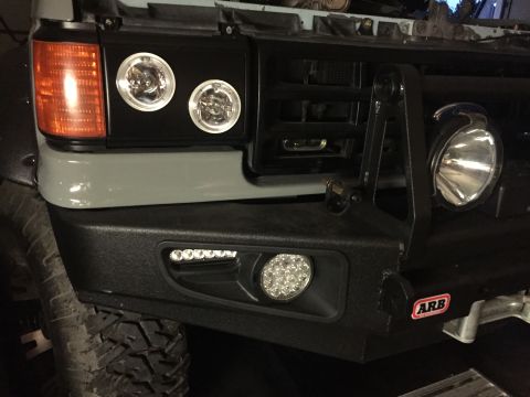 1988 Ford Bronco - The front bumper of a vehicle features two aftermarket LED fog lights and a large ARB badge. A mounted auxiliary driving light is visible o…