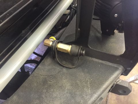 1988 Ford Bronco - A brass air chuck with a black rubber dust cap is mounted to the textured black bumper of a vehicle. The air chuck is connected to a yellow…