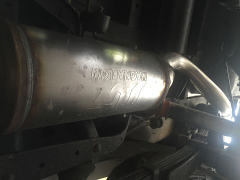 1988 Ford Bronco - A close-up view of the underside of a vehicle shows a stainless steel Magnaflow exhaust muffler and pipe. The muffler has the Magnaflow log…