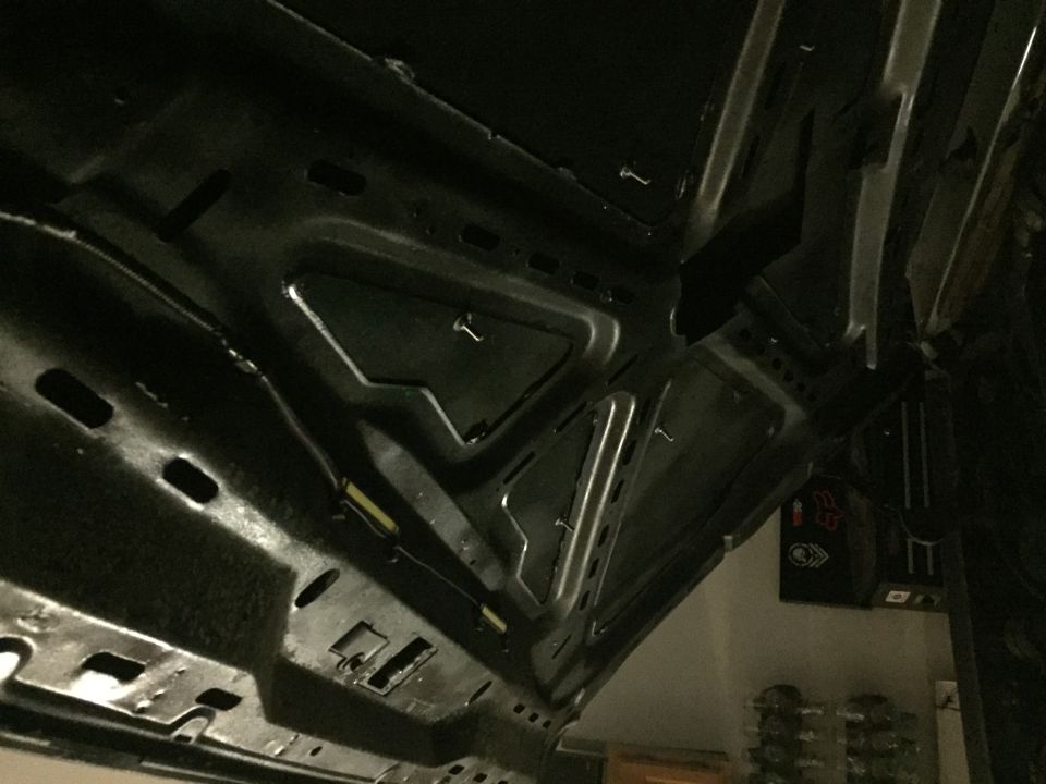 Underside of a black vehicle hood with structural beams and wiring.