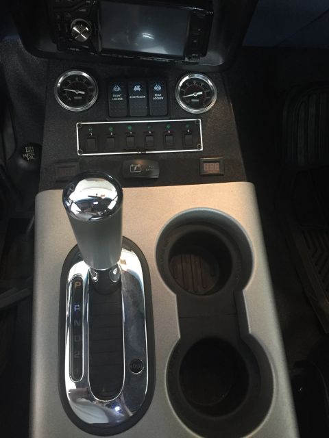 1988 Ford Bronco - Interior view of a vehicle's center console, featuring a chrome automatic gear shifter, auxiliary switches, gauges, and cup holders.
