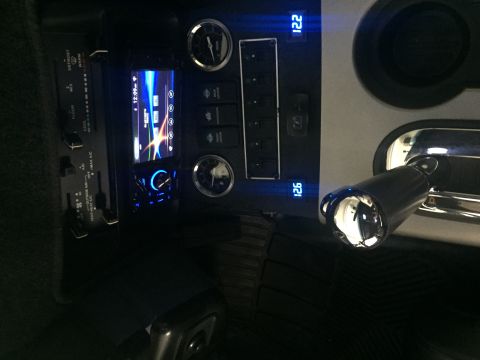 1988 Ford Bronco - The interior of a vehicle shows a modified dashboard with a digital screen, climate controls, and aftermarket gauges. A chrome-plated gear…