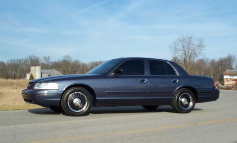 1998 Ford Crown Victoria - This sedan is parked on the side of a road with a rural background.