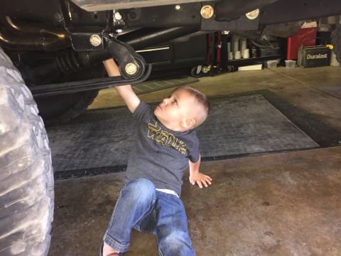 1988 Ford Bronco - A young boy in a Star Wars t-shirt and jeans reaches up to touch the underside of a vehicle, possibly a Ford Bronco, in a garage setting. T…
