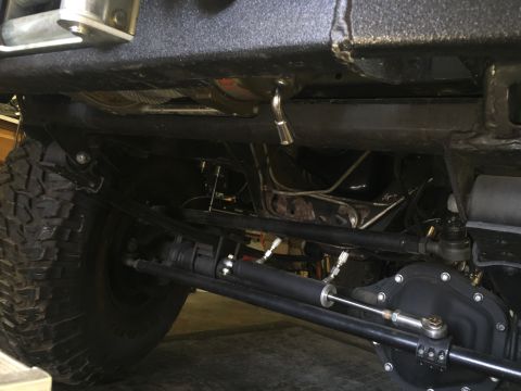 1988 Ford Bronco - Undercarriage view of a modified 4x4 vehicle, showing the front axle, steering components including a steering stabilizer, and part of a la…