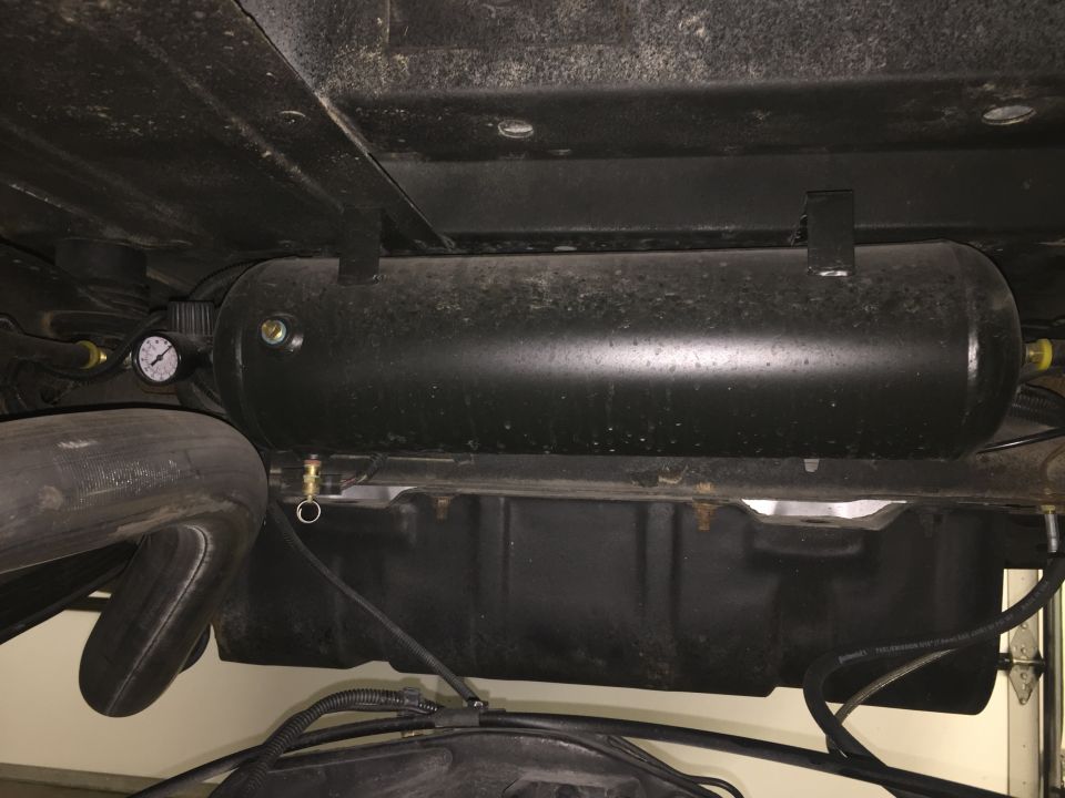 Underside view of a vehicle showing a black air tank and exhaust pipe.