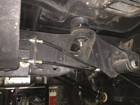 1988 Ford Bronco - The underside of a vehicle shows the frame with brake cables attached to a bracket. A large rubber mount is visible above the frame.