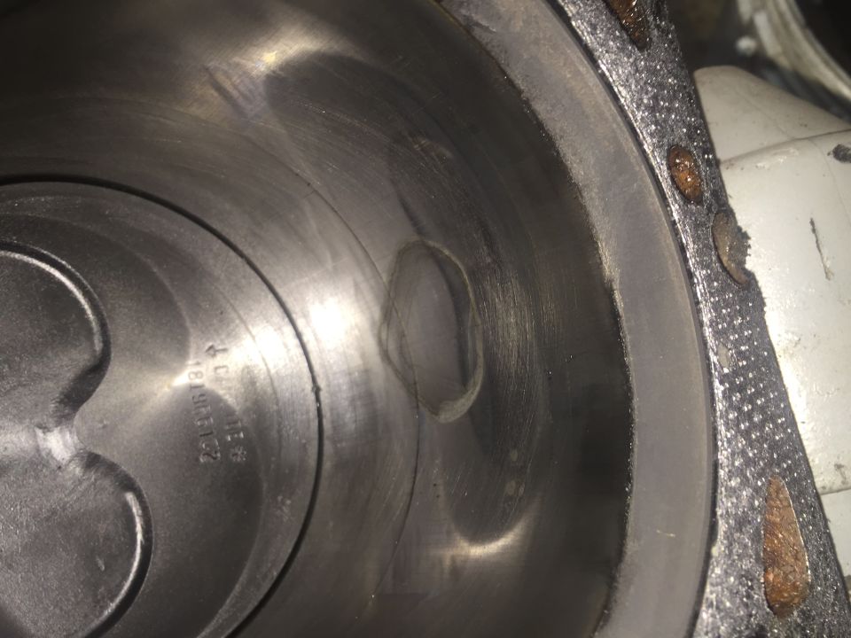 Close-up of an engine cylinder bore with visible scoring and a damaged section. A gasket is visible on the right